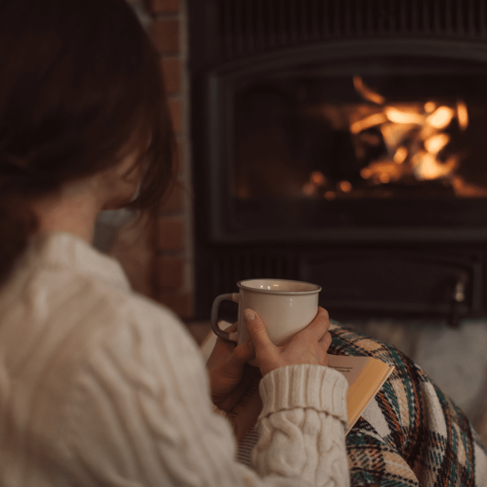 Woman being warmed by a gas fireplace with a hot cocoa serviced by Heaton Plumbing in Houston, Texas
